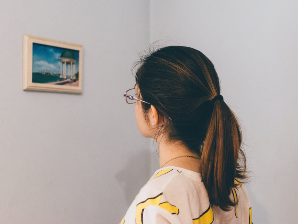 A young woman with glasses looking at a painting on a gallery wall.